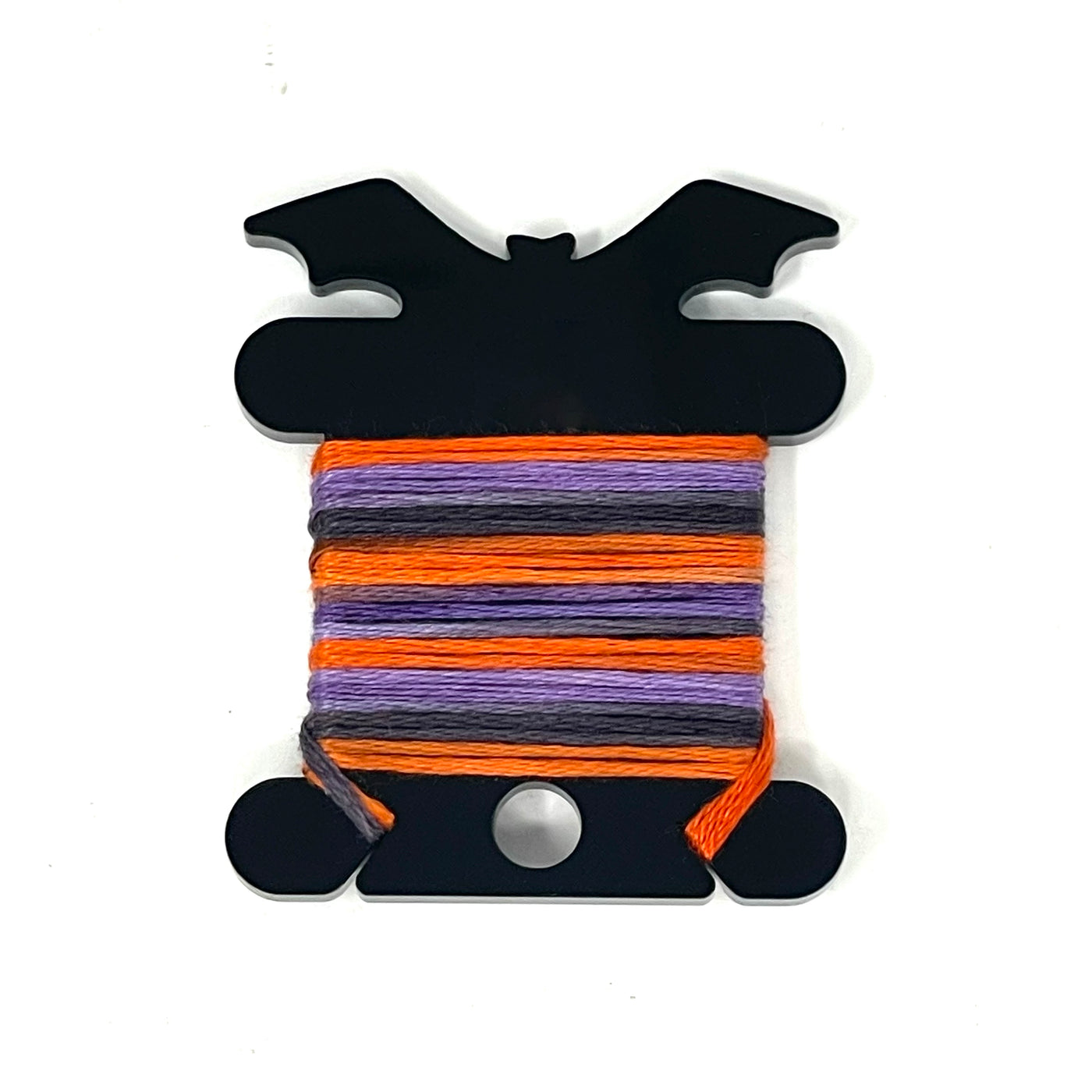 A black bat-shaped acrylic bobbin holder with embroidery floss wound around it. 