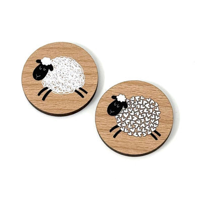 Two reversible sheep needle minders with one featuring a white sheep on a wooden background and the other with a black sheep design.