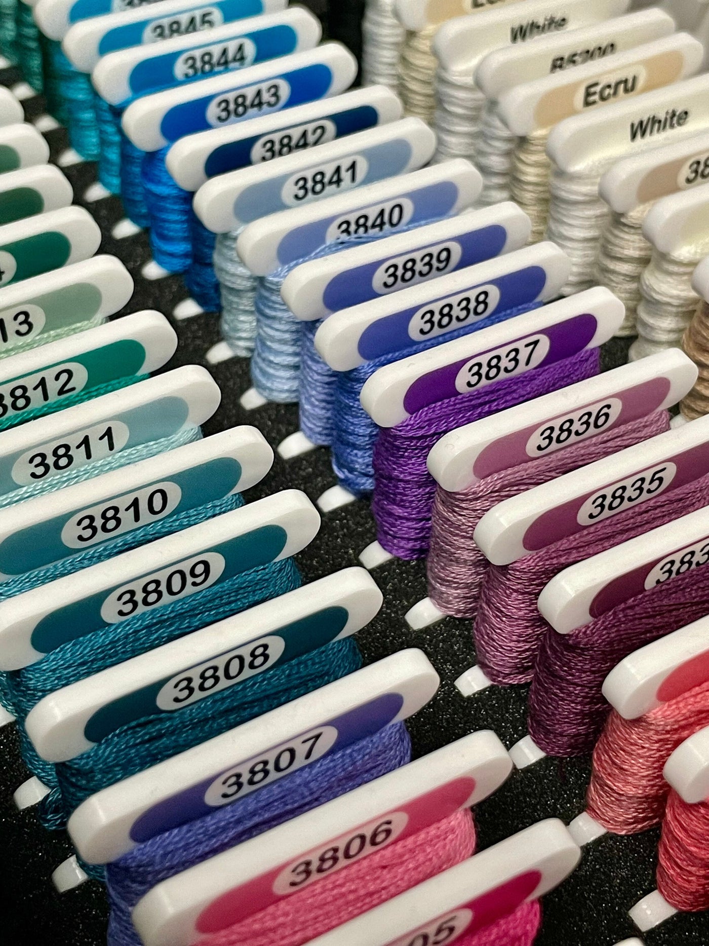 Premium DMC Acrylic cross stitch bobbins with thread wrapped on them in a foam insert. Made by Pip and Chip
