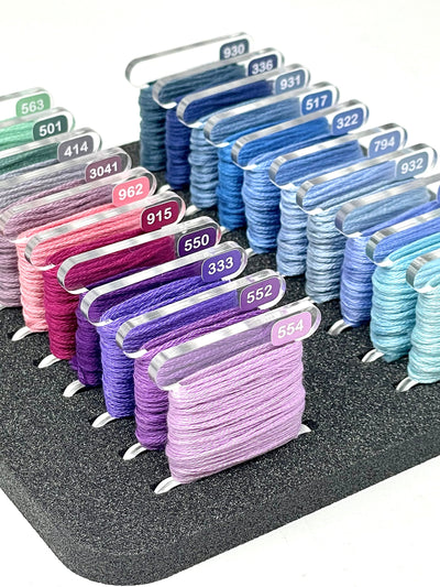 Clear Acrylic bobbins wrapped with DMC floss. Bobbins are stood in a foam insert and labelled with colour matched mini DMC vinyl labels by Pip and Chip